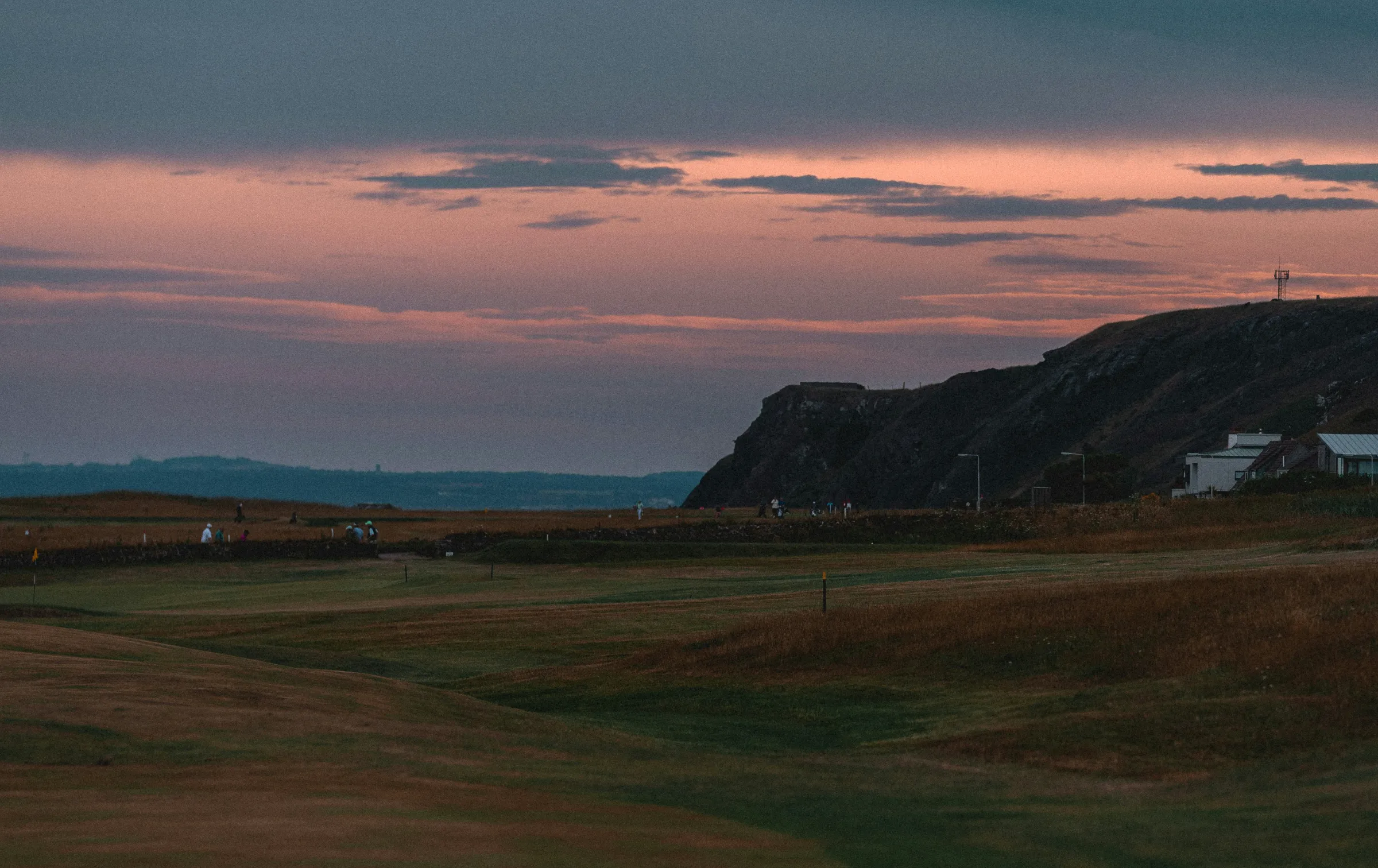 A links course at dusk, the fairway running out toward a clifftop under a pink and slate sky